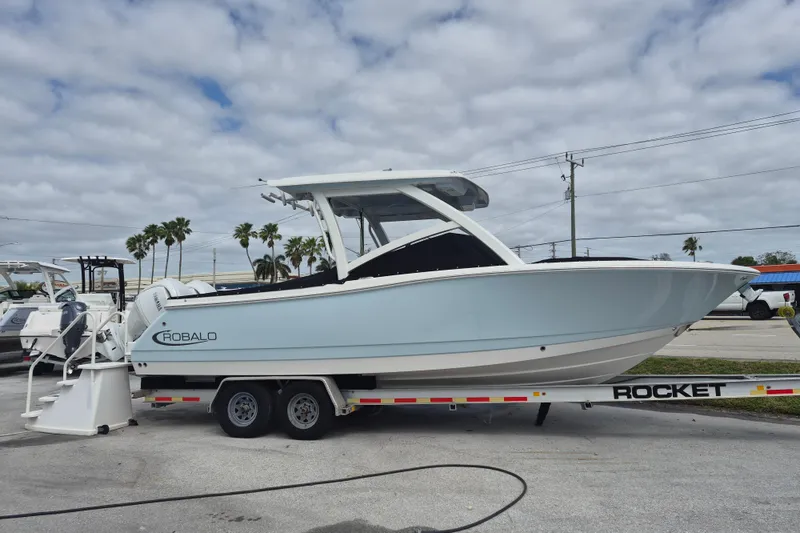 Slide: The Image of 2026 Robalo R277 Dual Console boat on trailer, parked outdoors under cloudy sky. - 12