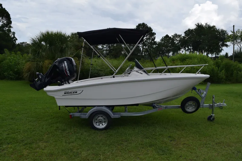 Slide: The Image of Boston Whaler 130 Super Sport 2026 on a trailer, with black bimini top and outboard motor. - 0