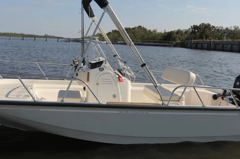 Slide: The Image of A 2026 Boston Whaler 150 Montauk on calm water. It features an open deck and a steering console. - 31
