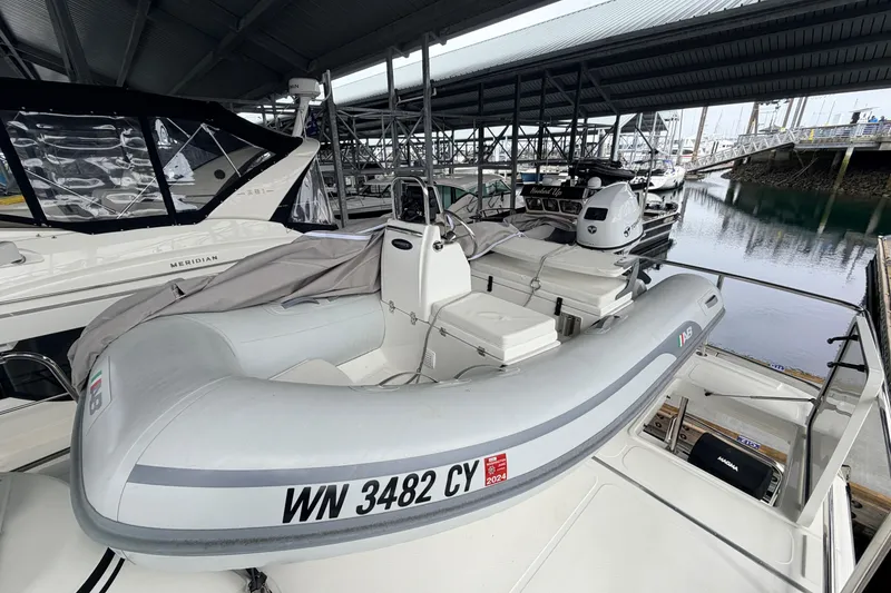 Slide: The Image of A 2022 American Tug 365 docked with an inflatable boat on deck under a covered marina. - 89