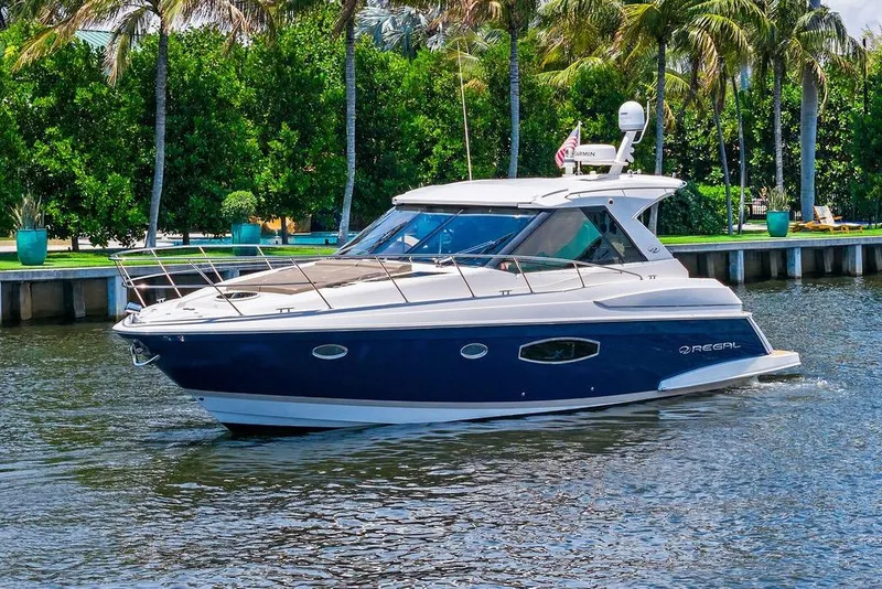 The Image of 2013 Regal 42 Sport Coupe yacht cruising on a scenic waterway with lush greenery. - 0