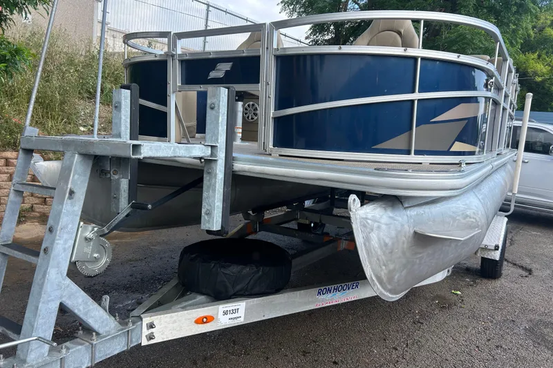 The Image of 2023 Starcraft LX 18 F pontoon boat on trailer, blue and silver design. - 0