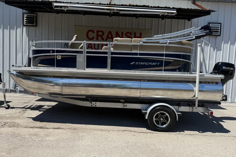 Slide: The Image of 2023 Starcraft LX 18 F pontoon boat on trailer, parked outside a building. - 17