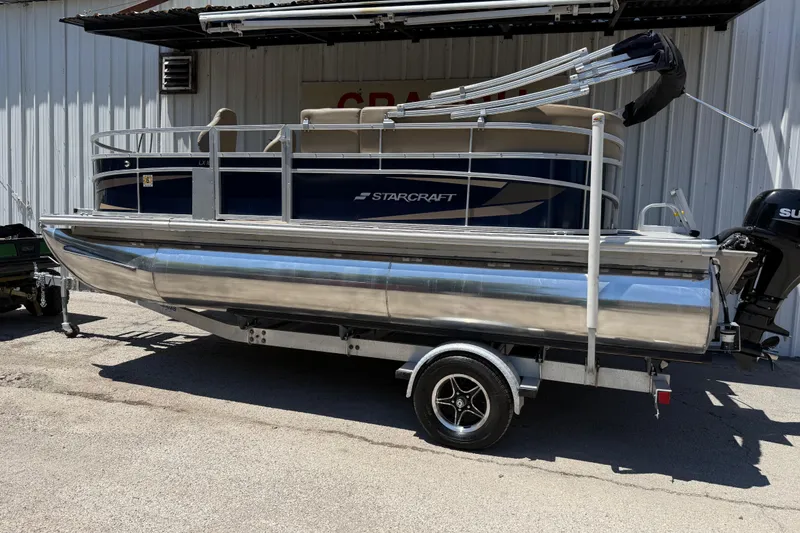 Slide: The Image of 2023 Starcraft LX 18 F pontoon boat on trailer, parked outdoors. - 18