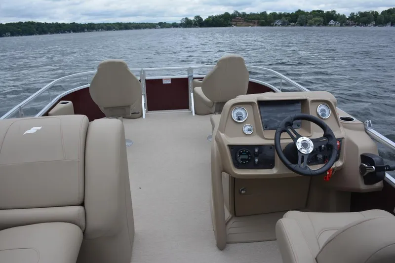 Slide: The Image of Manufacturer Provided Image: 2023 Starcraft LX 18 F pontoon boat interior with beige seating and steering console on a lake. - 3
