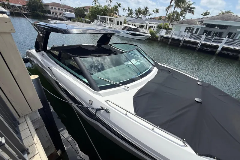 Slide: The Image of 2021 Cruisers Yachts 38 GLS OB docked by waterfront homes, featuring sleek design and covered deck. - 7