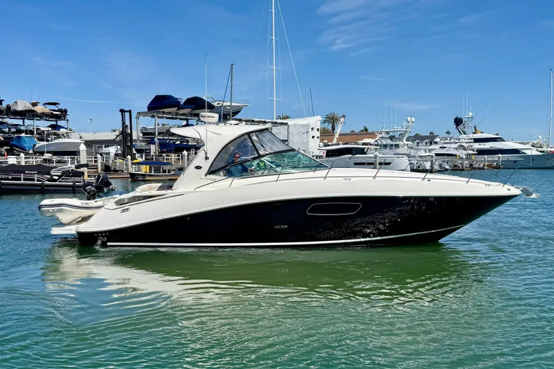 The Image of 2009 Sea Ray Sundancer 350 yacht cruising in a marina under a clear blue sky. - 0