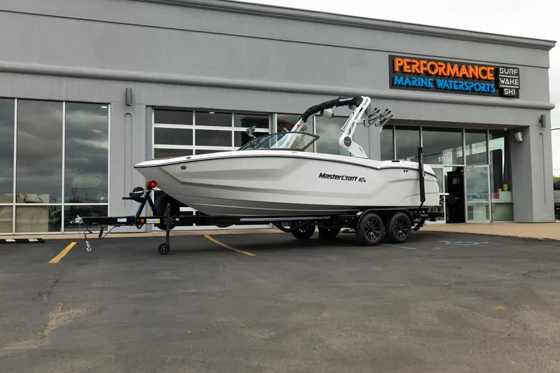 The Image of 2026 MasterCraft NXT23 boat on trailer outside Performance Marine Watersports dealership. - 1