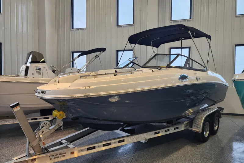 The Image of 2026 Stingray 211 DC boat on trailer in showroom, featuring sleek design and canopy. - 0