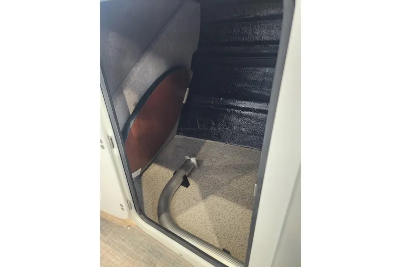 Slide: The Image of Interior storage compartment of 2026 Stingray 211 DC boat, featuring carpeted flooring and a wooden panel. - 37