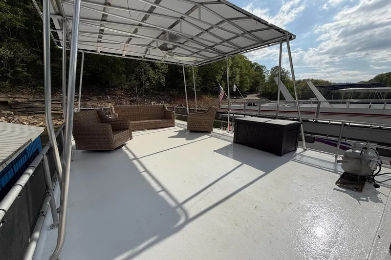 Slide: The Image of 1989 Sumerset 14x63 houseboat deck with wicker furniture and canopy, docked by a wooded shoreline. - 28