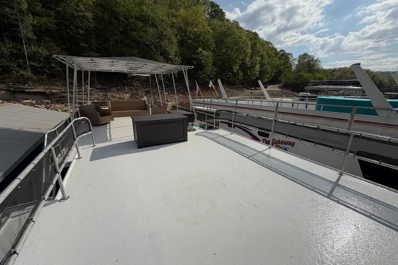 Slide: The Image of 1989 Sumerset 14x63 houseboat deck with seating, docked near lush green shoreline. - 31