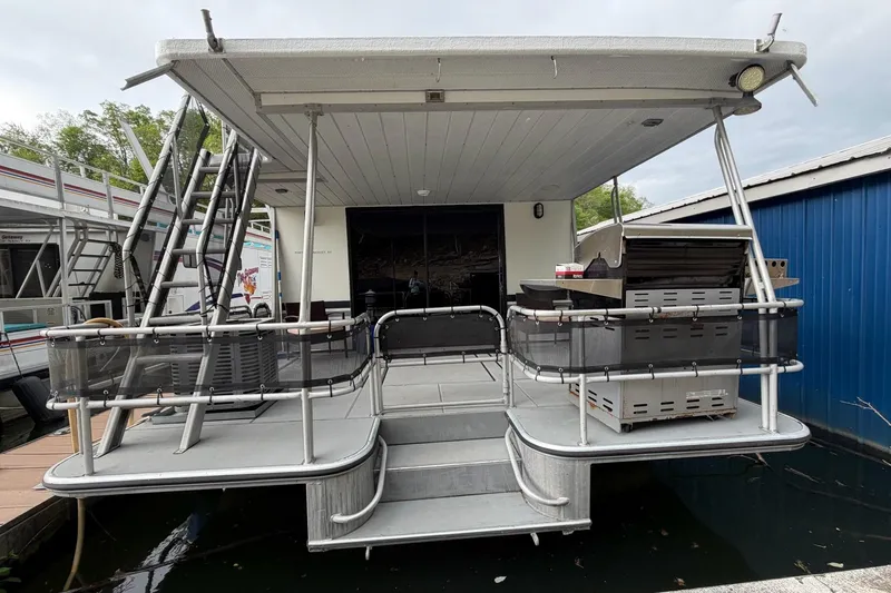 Slide: The Image of 1989 Sumerset 14x63 houseboat with outdoor deck and grill, docked beside a blue building. - 46