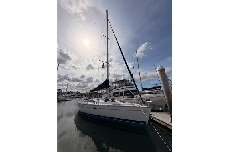 Slide: The Image of 1998 Hunter Legend 40.5 sailboat docked under a cloudy sky, reflecting on calm water. - 2
