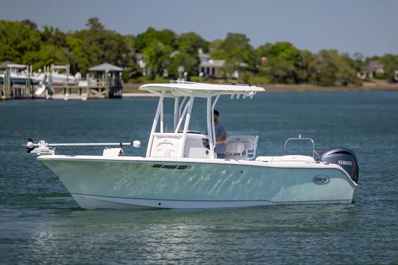 Slide: The Image of 2024 Sea Hunt Ultra 234 boat cruising on a calm lake with lush green shoreline. - 5