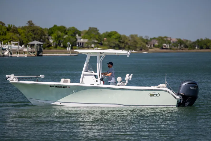 Slide: The Image of 2024 Sea Hunt Ultra 234 boat cruising on a calm lake with a person at the helm. - 7