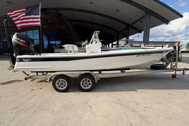 Slide: The Image of 2012 BlackJack 224 boat on trailer with Suzuki engine, parked under a metal canopy. - 3