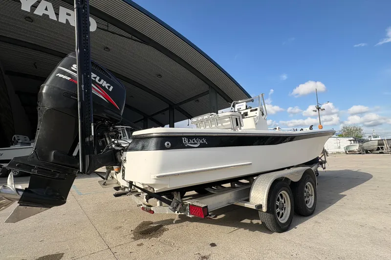 Slide: The Image of 2012 BlackJack 224 boat on trailer with Suzuki outboard motor, parked near a large building. - 4