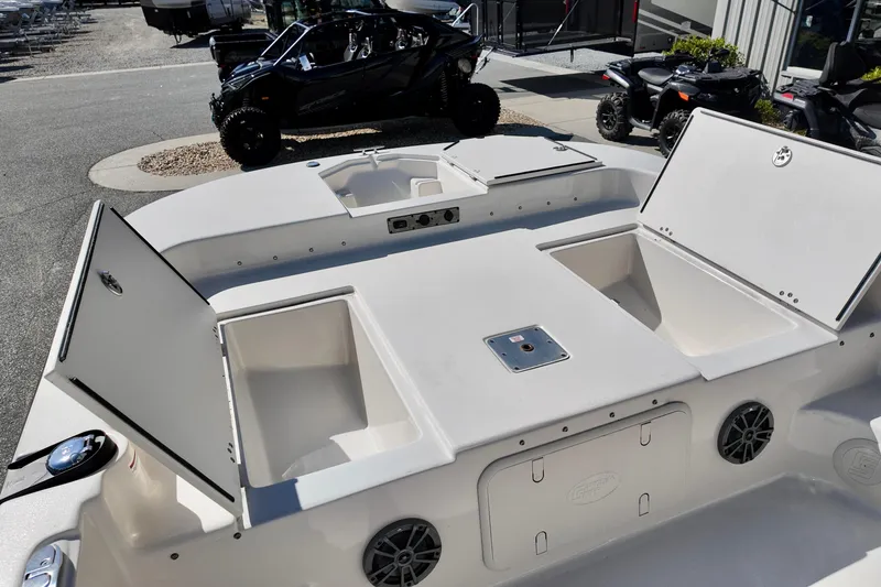 Slide: The Image of 2026 Carolina Skiff 21 LS boat with open storage compartments, parked near off-road vehicles. - 5