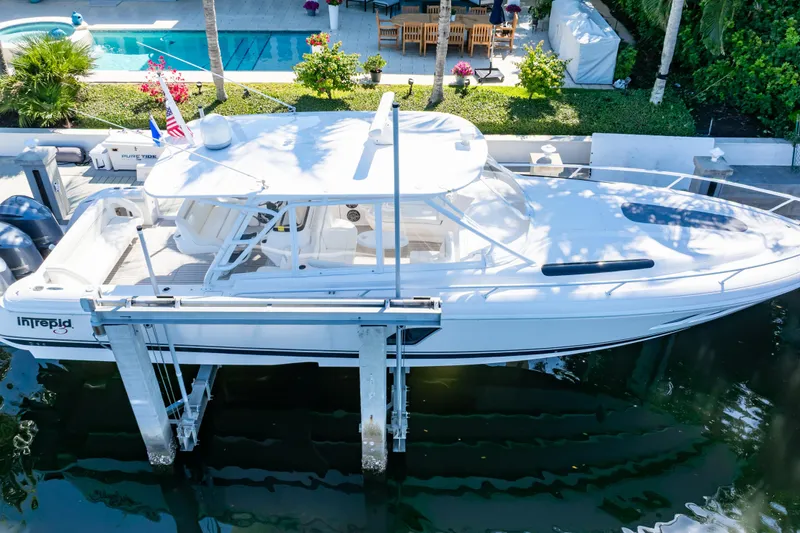 Slide: The Image of 2016 Intrepid 400 Cuddy boat docked near a poolside patio with lush greenery. - 13