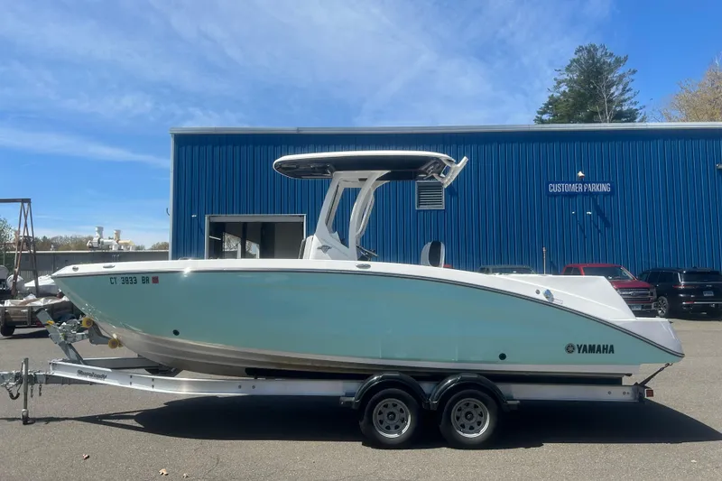 The Image of 2024 Yamaha Boats 252 FSH Sport on trailer, parked outside blue building. - 0