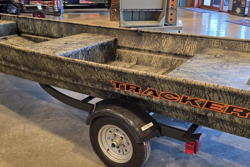 Slide: The Image of 2026 Tracker Grizzly 15 Jon boat on trailer, camo design, displayed indoors. - 3