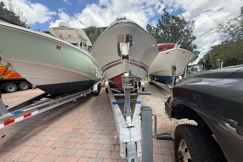 Slide: The Image of 2001 Wellcraft 29 Scarab Sport Open on trailer, surrounded by other boats, under a partly cloudy sky. - 14