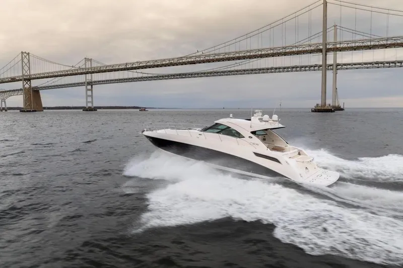 Slide: The Image of 2013 Sea Ray Sundancer 540 yacht cruising under a large bridge on open water. - 2