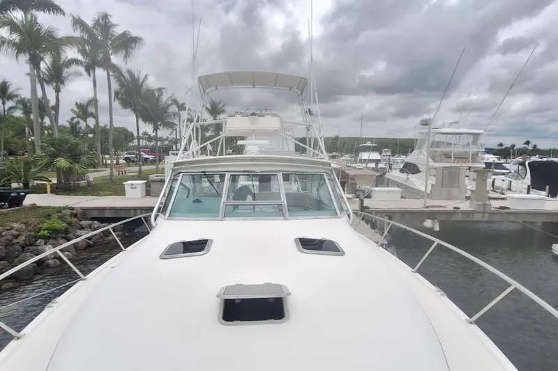Slide: The Image of 1998 Tiara Yachts 4100 Open docked at marina, surrounded by palm trees and cloudy sky. - 7