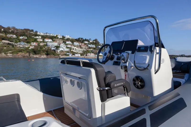 Slide: The Image of 2026 Brig Eagle 6.7 boat interior with steering wheel, dashboard, and scenic coastal view. - 6