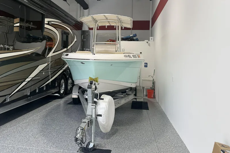 Slide: The Image of 2021 Robalo R200 Center Console boat in a garage beside a large RV. - 2