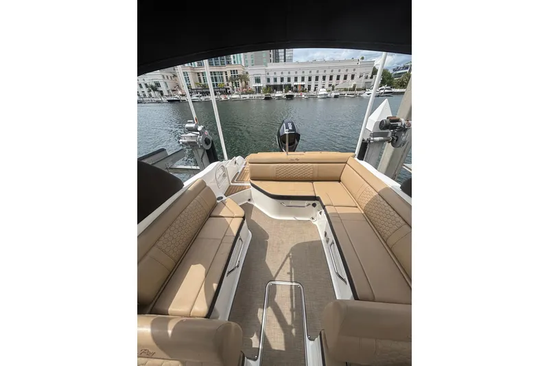 Slide: The Image of 2019 Sea Ray SDX 270 Outboard boat interior with tan seating, docked by waterfront buildings. - 9