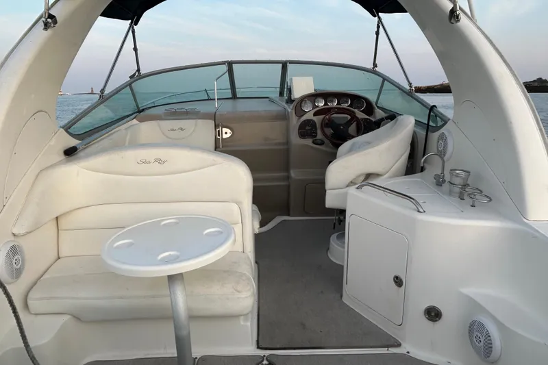 Slide: The Image of 2005 Sea Ray Sundancer 280 boat interior with helm, seating, and table on calm water. - 6