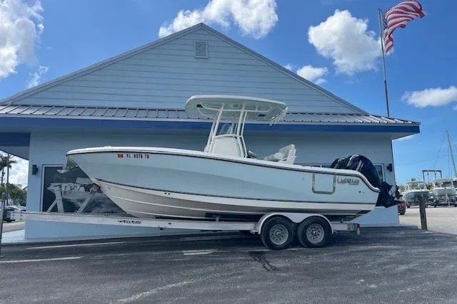 The Image of 2021 Mako 236 Center Console boat on trailer, parked outside a building with American flag. - 1
