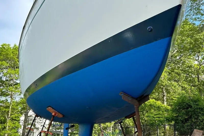 Slide: The Image of 1984 Pearson 34 sailboat hull, blue and white, on stands in a wooded area. - 2