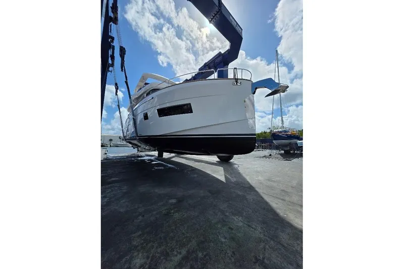 Slide: The Image of 2024 Sirena 58 Flybridge MY yacht being lifted at a marina under a bright sky. - 87