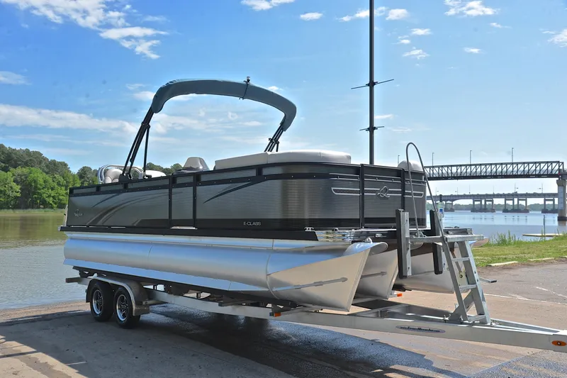 Slide: The Image of 2022 Qwest E822 pontoon boat on trailer by a river with bridge in background. - 16