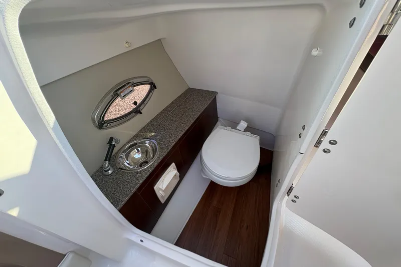 Slide: The Image of 2015 Chaparral 246 SSi boat bathroom with toilet, sink, and porthole window. - 17