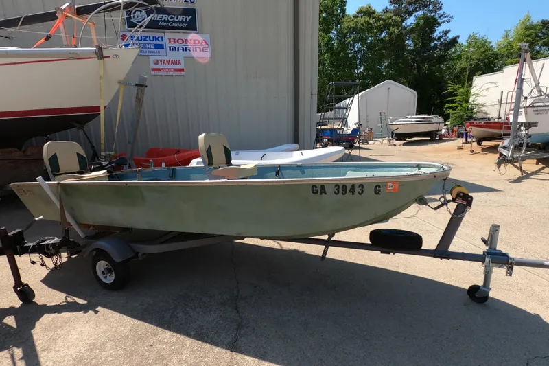 The Image of 1969 Thundercraft 14 boat on trailer, parked outdoors near marine dealership signs. - 1