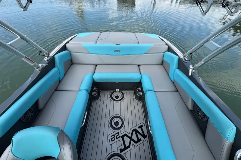 Slide: The Image of 2017 MasterCraft NXT22 boat interior with blue and gray seating, docked on calm water. - 15