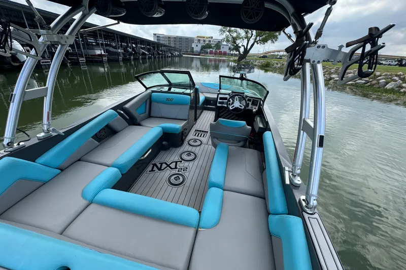 Slide: The Image of 2017 MasterCraft NXT22 boat interior with blue and gray seating, docked by the water. - 16