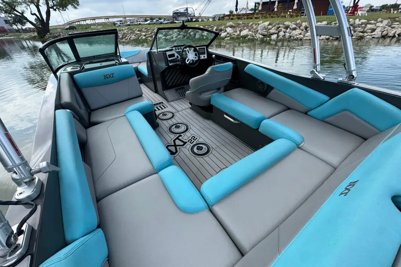 Slide: The Image of 2017 MasterCraft NXT22 boat interior with blue and gray seating, docked by a lake. - 17
