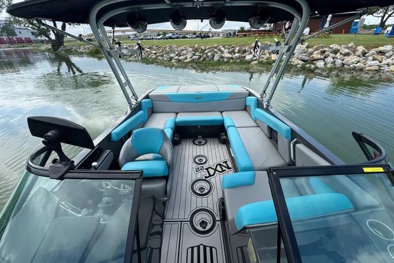 Slide: The Image of 2017 MasterCraft NXT22 boat interior with blue and gray seating, docked by a rocky shoreline. - 9
