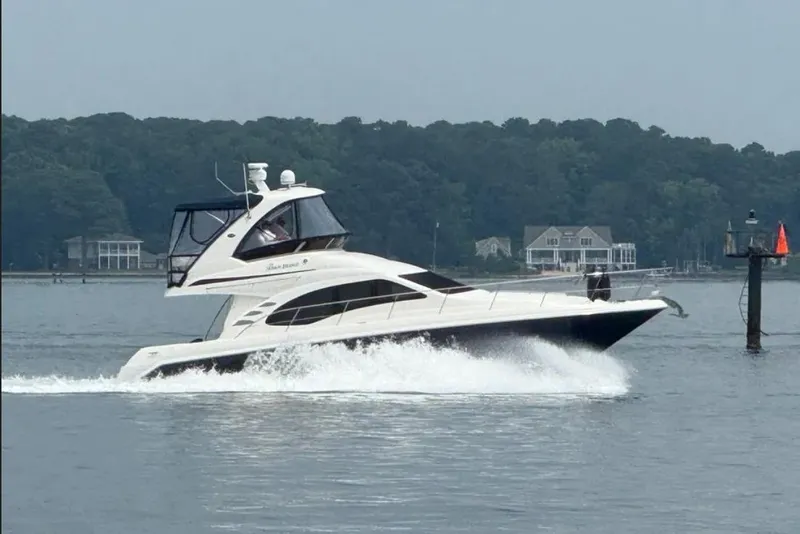 Slide: The Image of 2007 Sea Ray 44 Sedan Bridge cruising on a calm lake with houses in the background. - 1