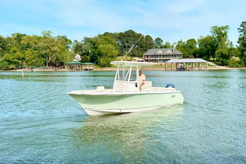 Slide: The Image of 2020 Sea Hunt Ultra 234 boat cruising on a serene lake near a lakeside house. - 2