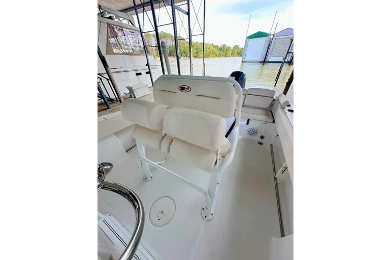 Slide: The Image of 2020 Sea Hunt Ultra 234 boat interior with white seating and steering wheel, docked by the water. - 4