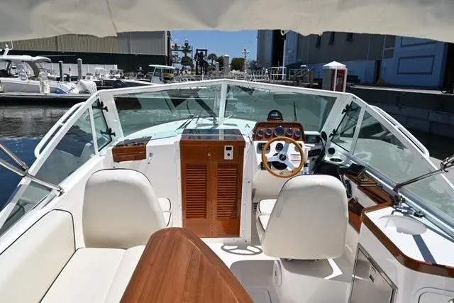 Slide: The Image of 2013 Hunt Yachts Harrier 25 interior with helm, wooden accents, and seating at a marina. - 9