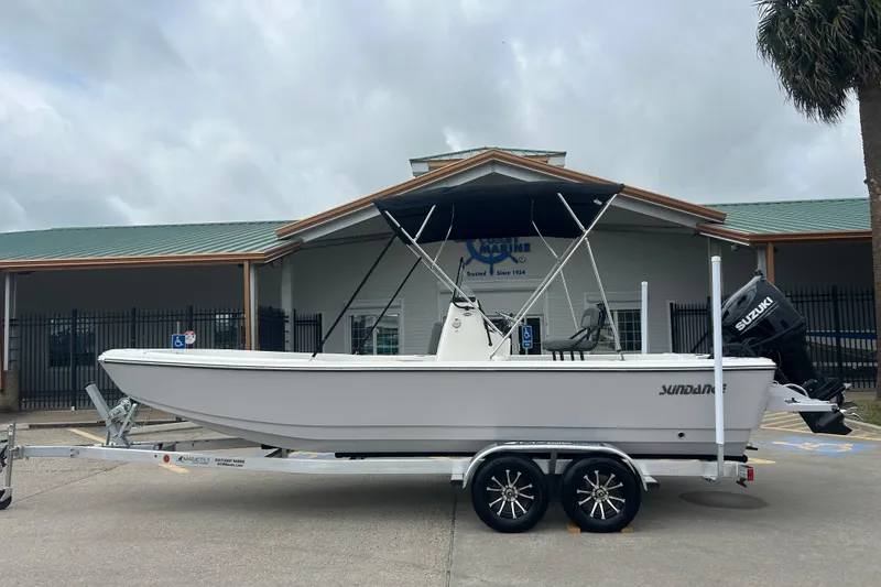 The Image of 2026 Sundance DX22 boat on trailer, parked outside a marine dealership. - 0