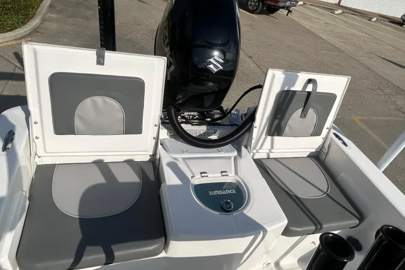 Slide: The Image of 2026 Sundance DX22 boat interior with gray seating and Suzuki engine in a parking lot. - 17