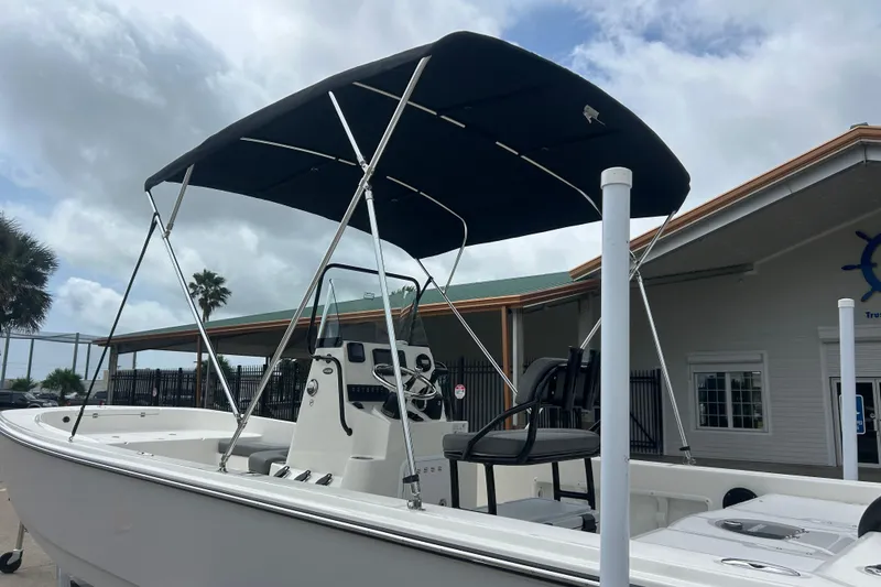 Slide: The Image of 2026 Sundance DX22 boat with canopy, parked near a building under cloudy skies. - 2